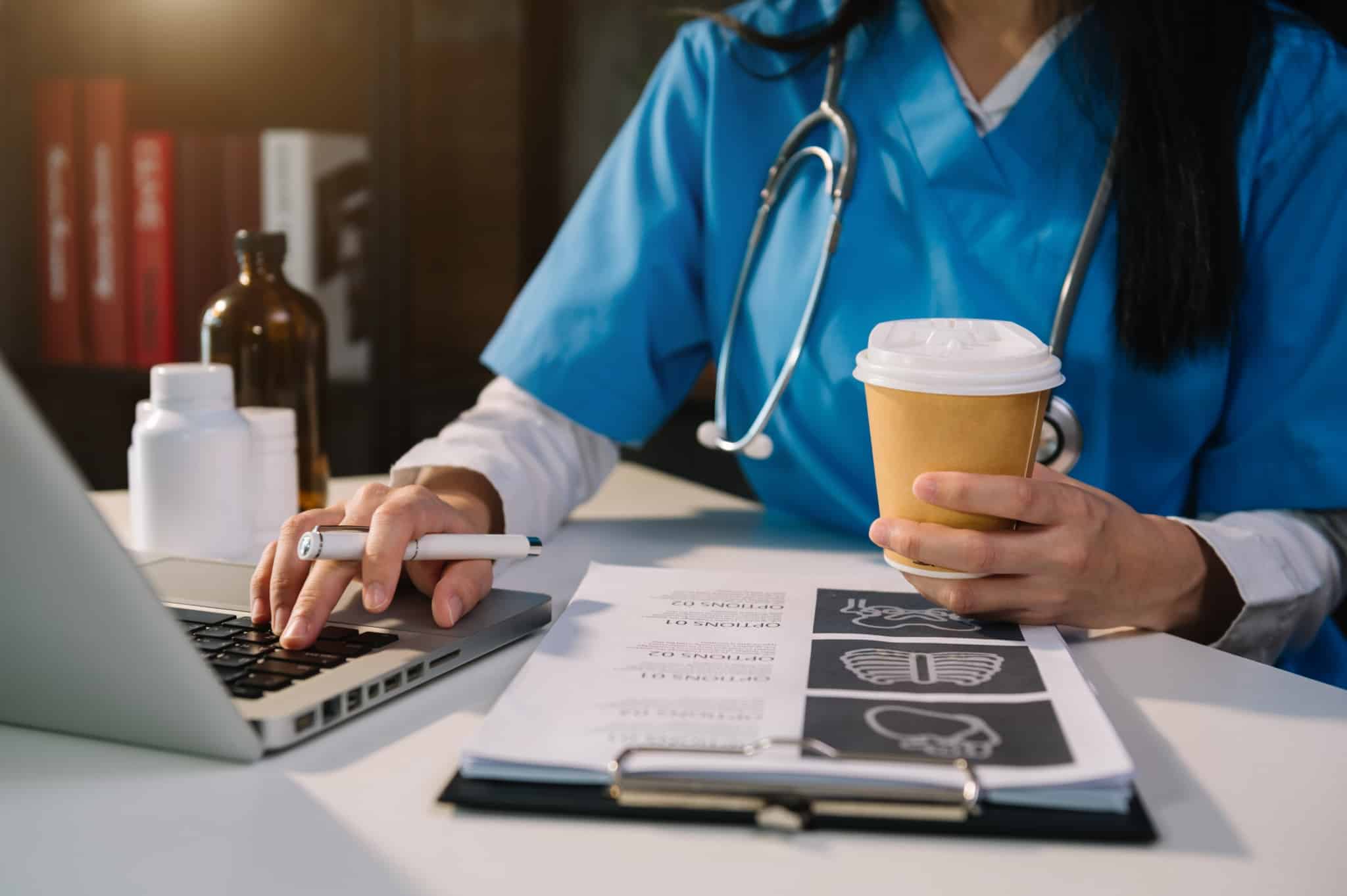 Medical professional holding a cup of coffee while typing on a laptop
