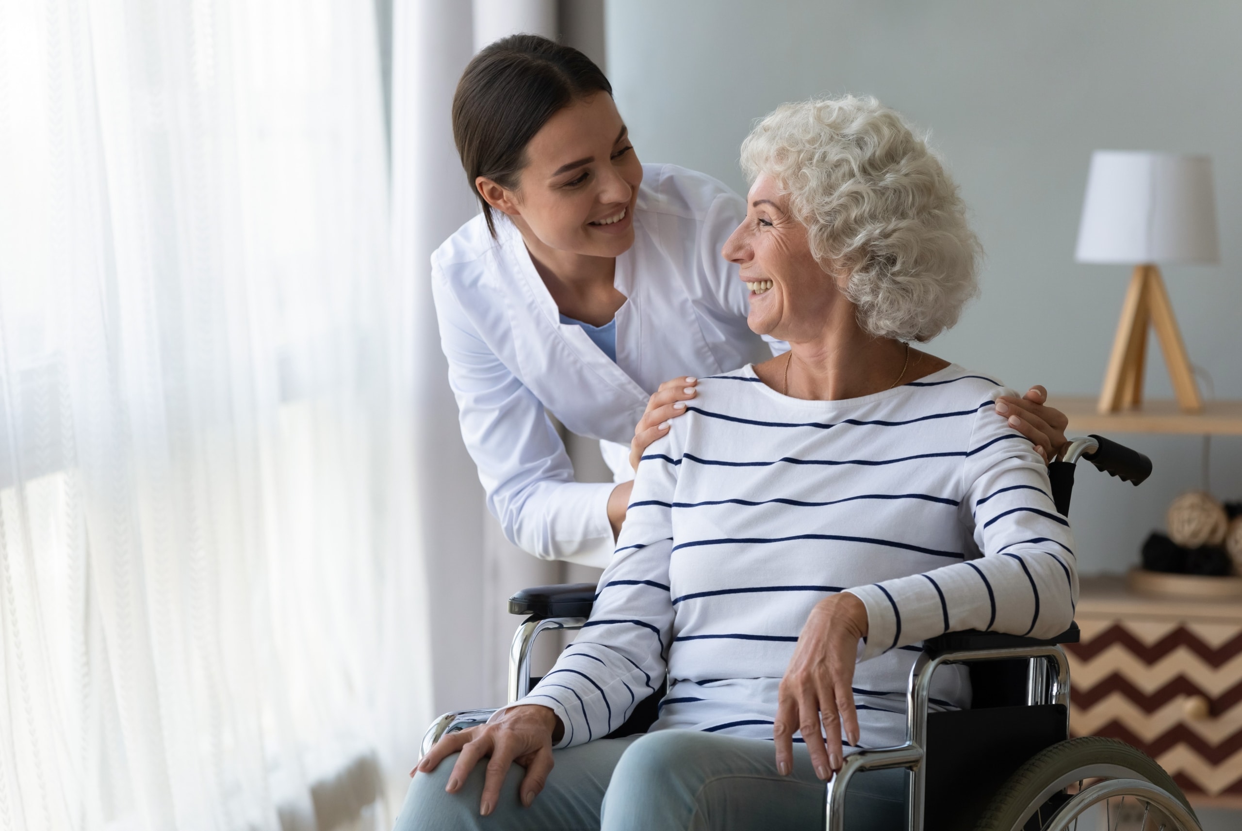 Medical professional smiling at an elderly woman in a wheelchair