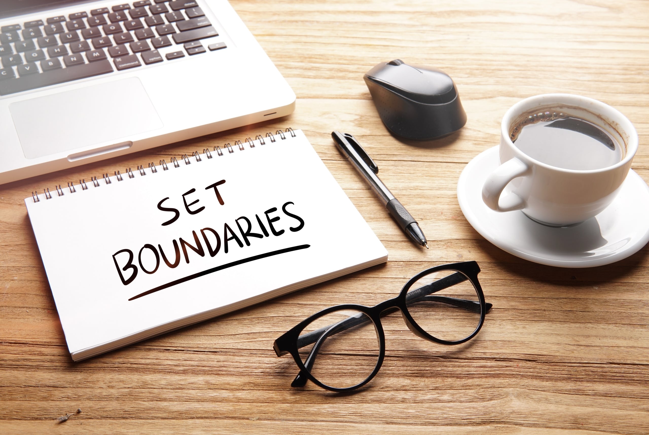 A pad of paper that says set boundaries next to a cup of coffee and other items