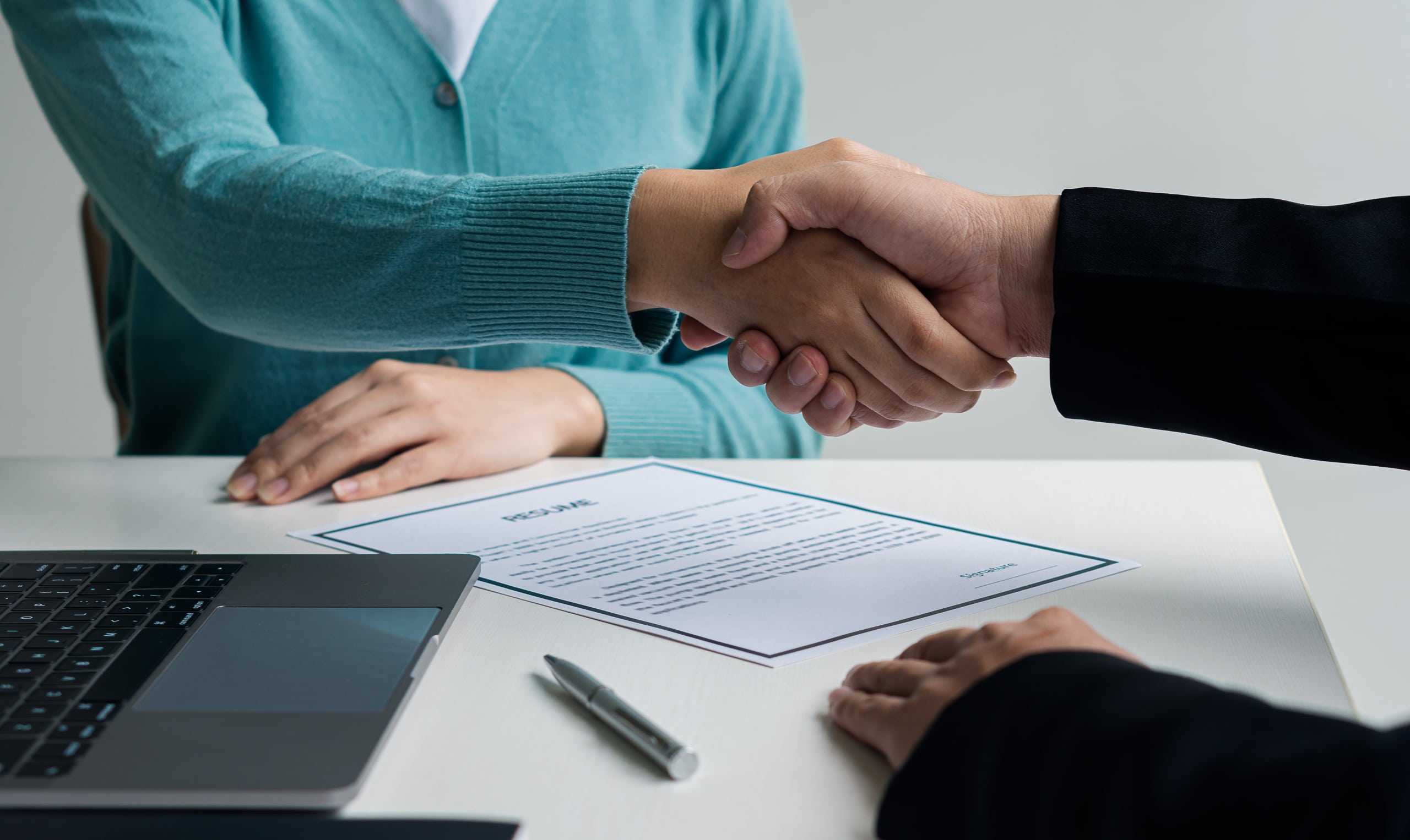 Close up of two professionals shaking hands over a resume