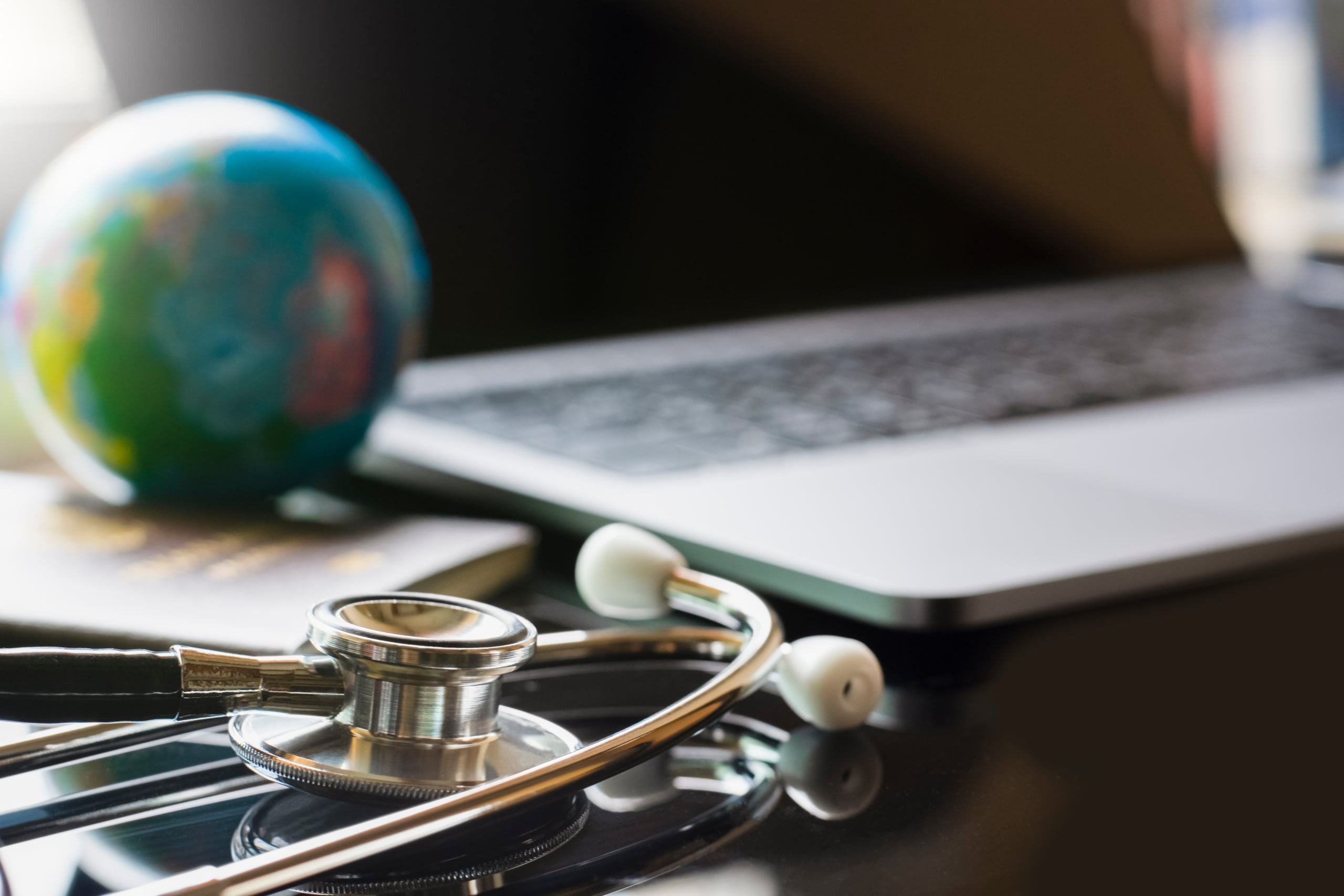 Close up of a laptop, stethoscope, and mini globe