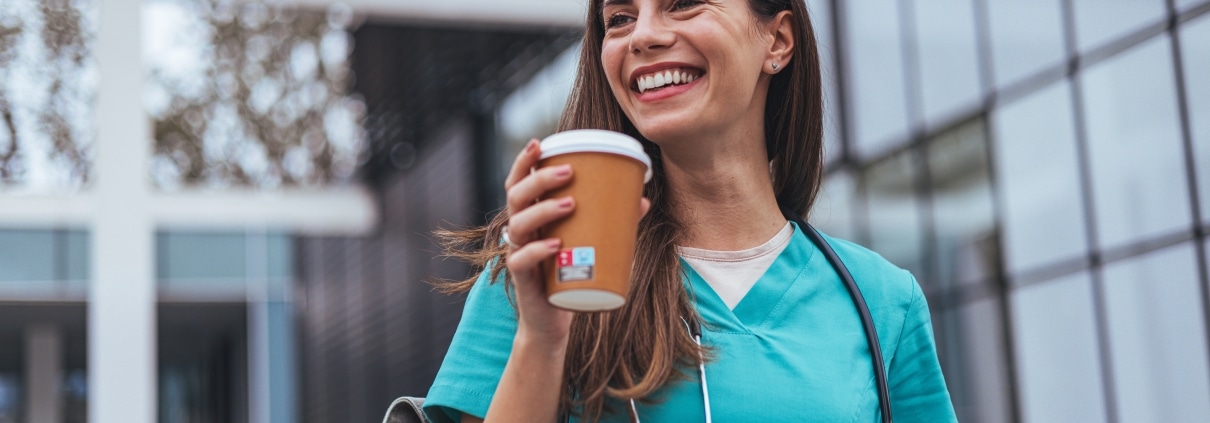 Smiling nurse holding a cup of coffee outside