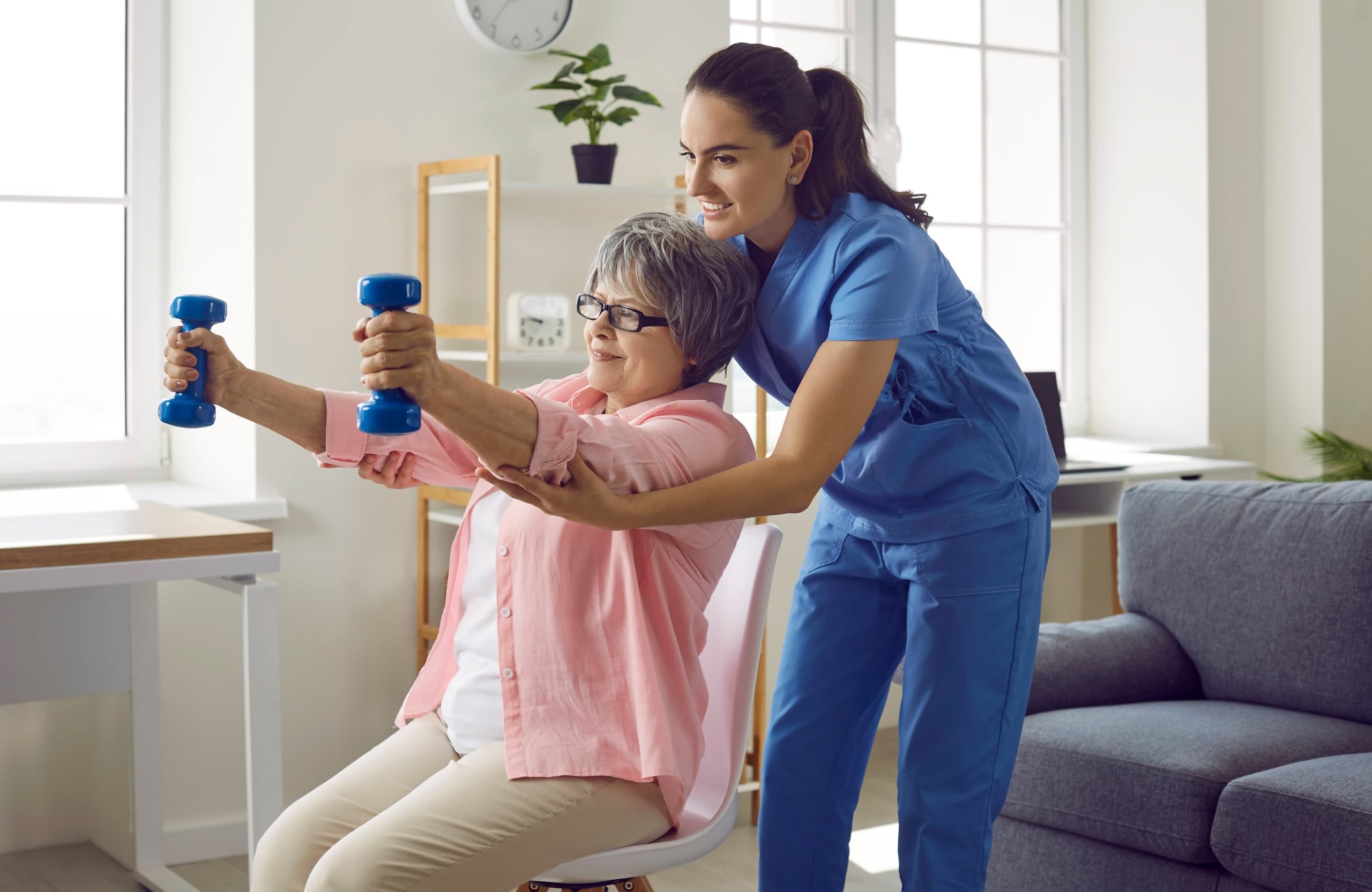Physical therapy professional helping an older woman lift weights