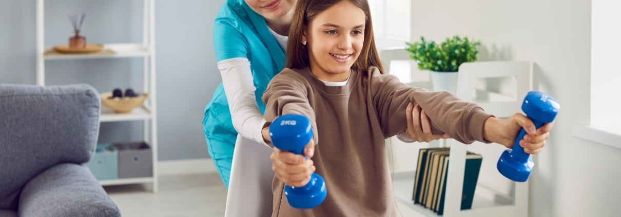Physical therapy professional helping a young girl lift weights