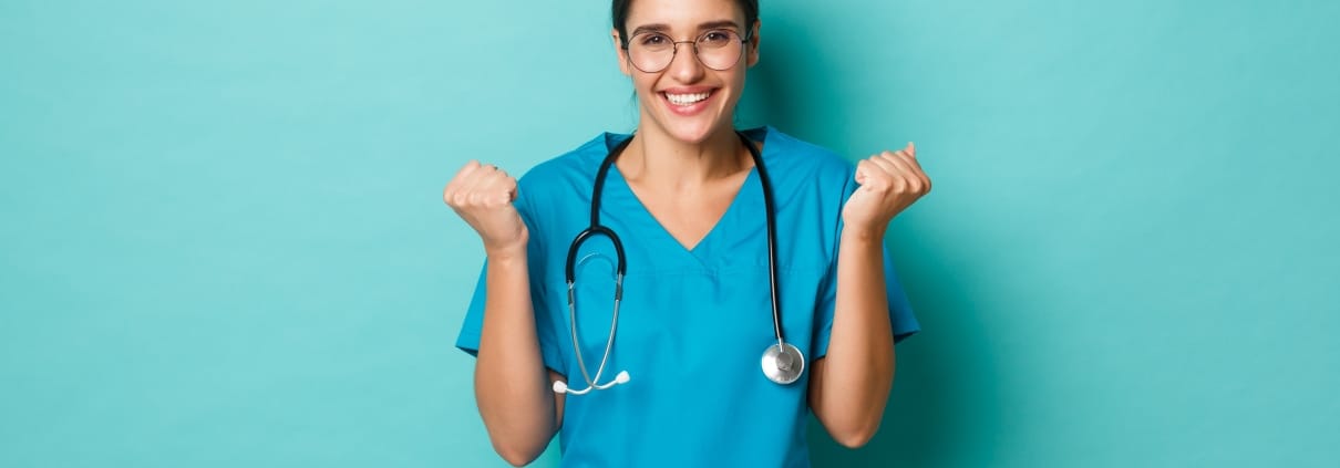 Smiling nurse holding her fists up against a solid backdrop