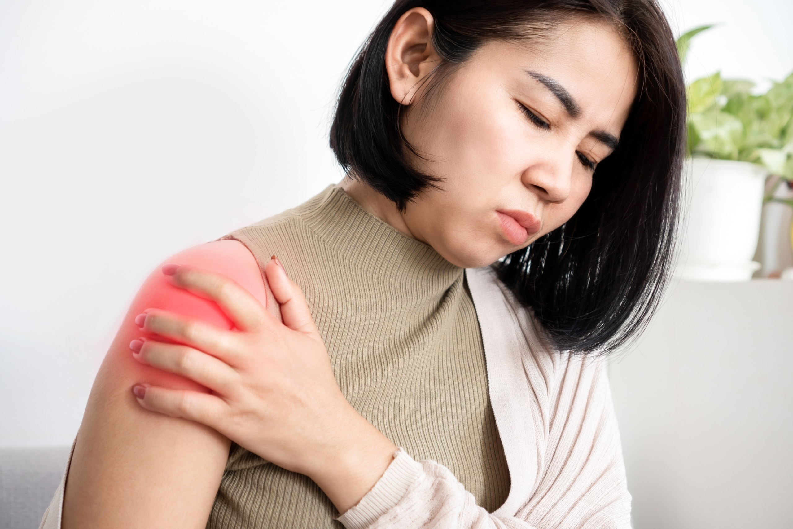 Asian woman gripping her shoulder in pain