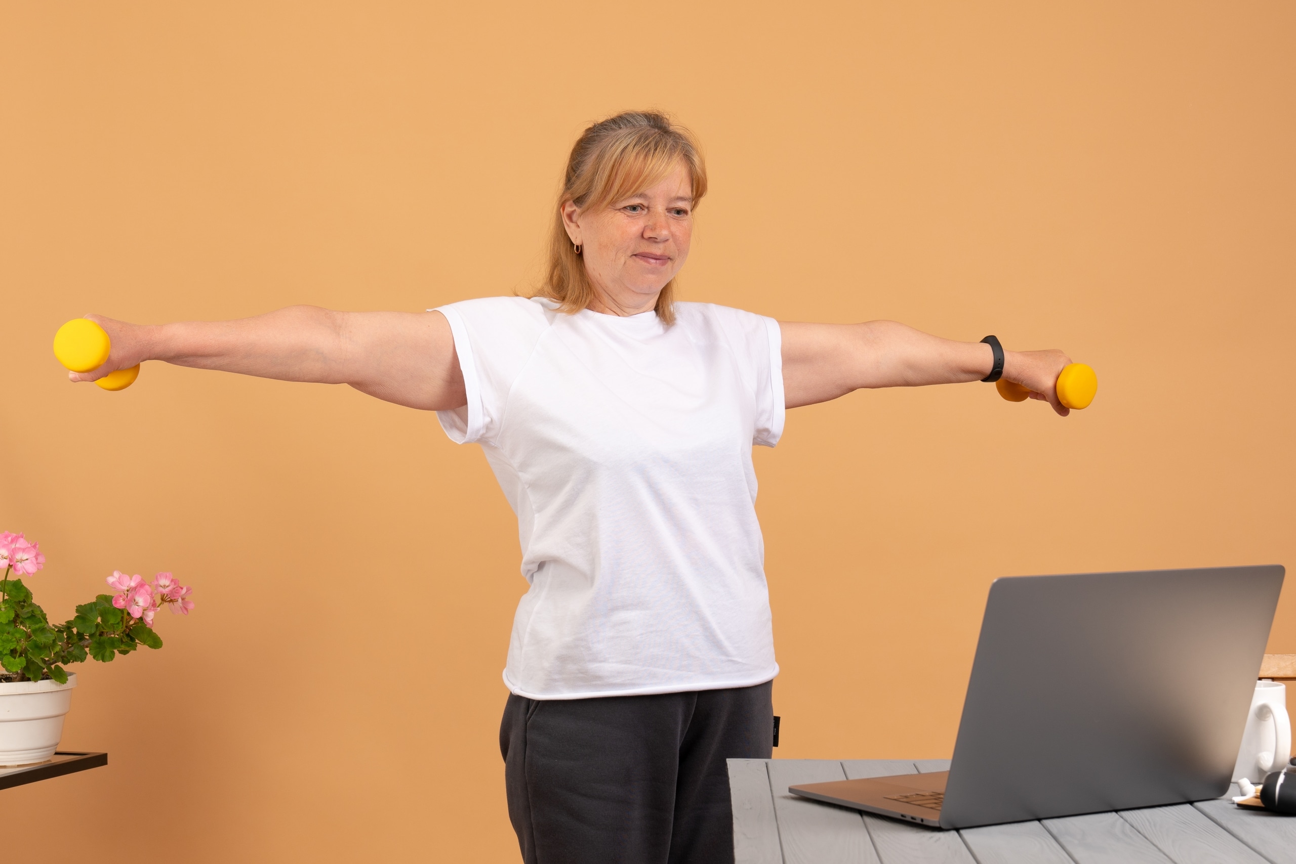 Woman lifting hand weights at home in front of her laptop