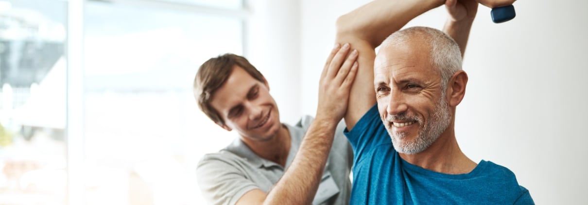 Older man smiling and lifting hand weights in physical therapy