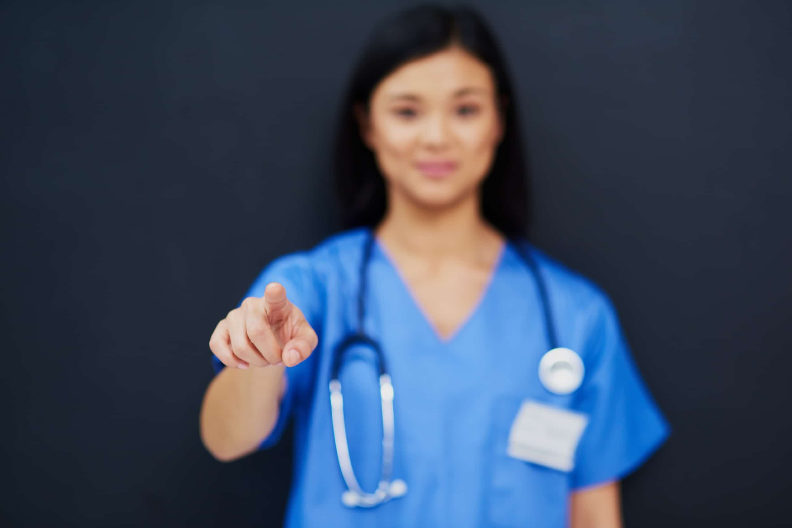 Asian nurse in scrubs pointing toward the camera