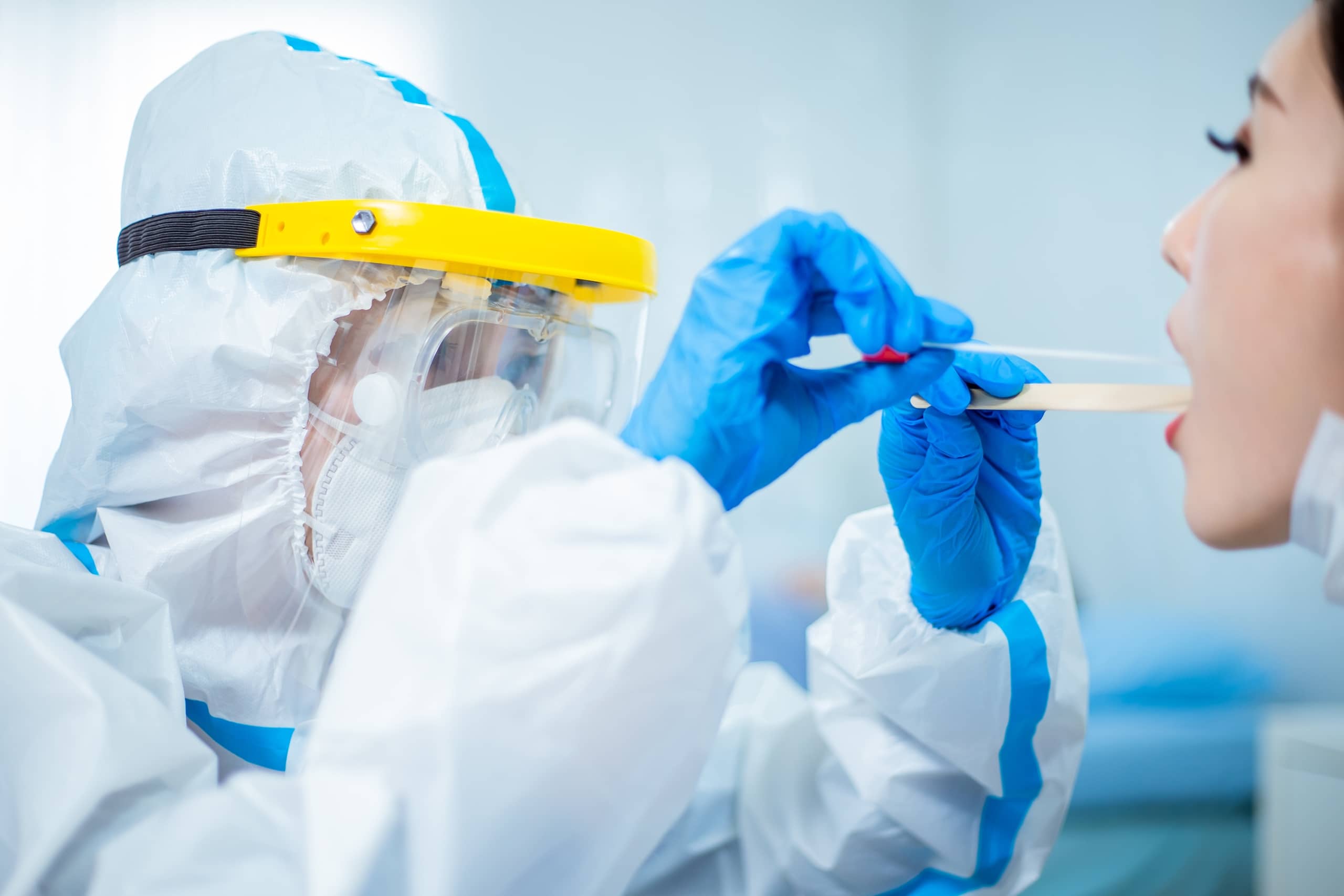 Medical professional in protective gear taking a throat swab from a woman