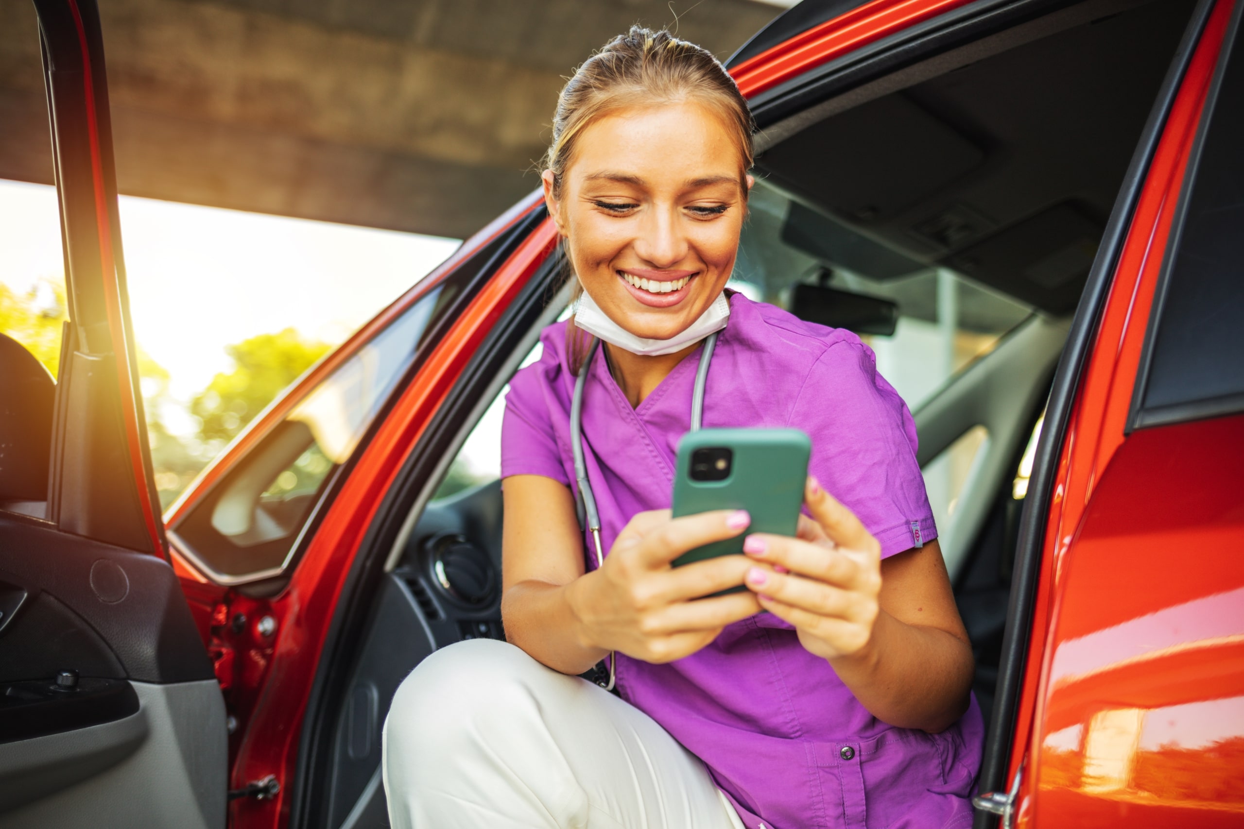 Smiling travel nurse sitting in her car and looking at her phone