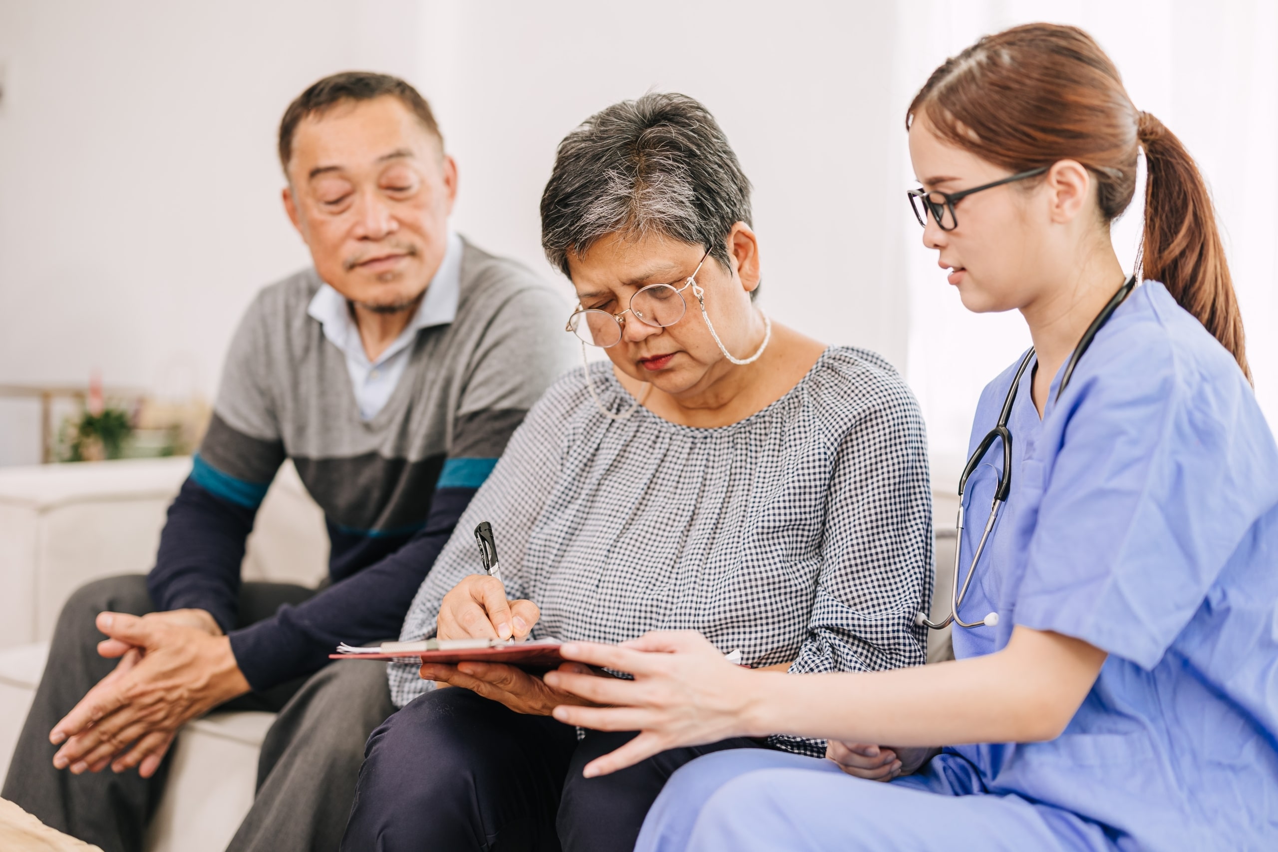 Elderly woman signing paperwork with a young Asian nurse