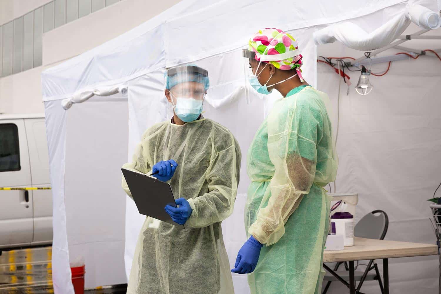 Medical professionals in PPE gear next to tents